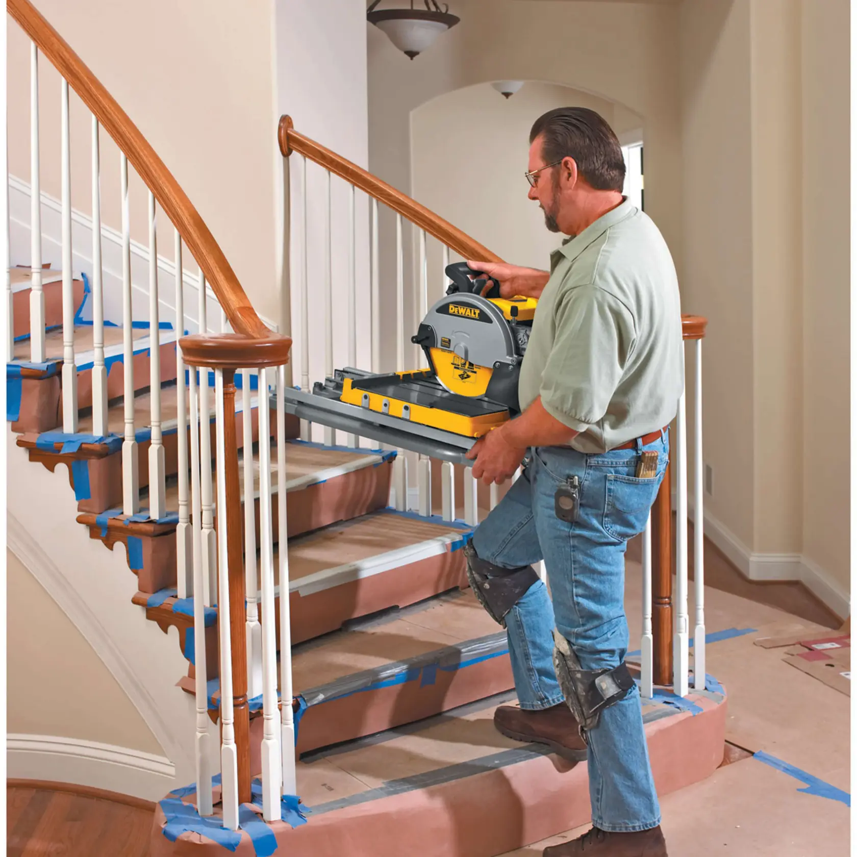Une personne portant des genouillères transporte une scie à carrelage DEWALT D24000 dans un escalier. Les marches sont couvertes de papier de protection et de ruban adhésif bleu. L’environnement semble être intérieur lors de travaux de rénovation.