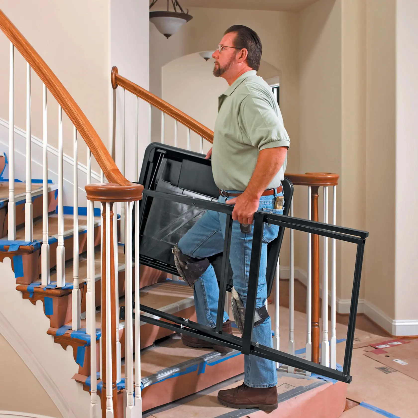 Personne portant une structure de support pour scie à carrelage DEWALT D24000 dans un escalier couvert de protections.