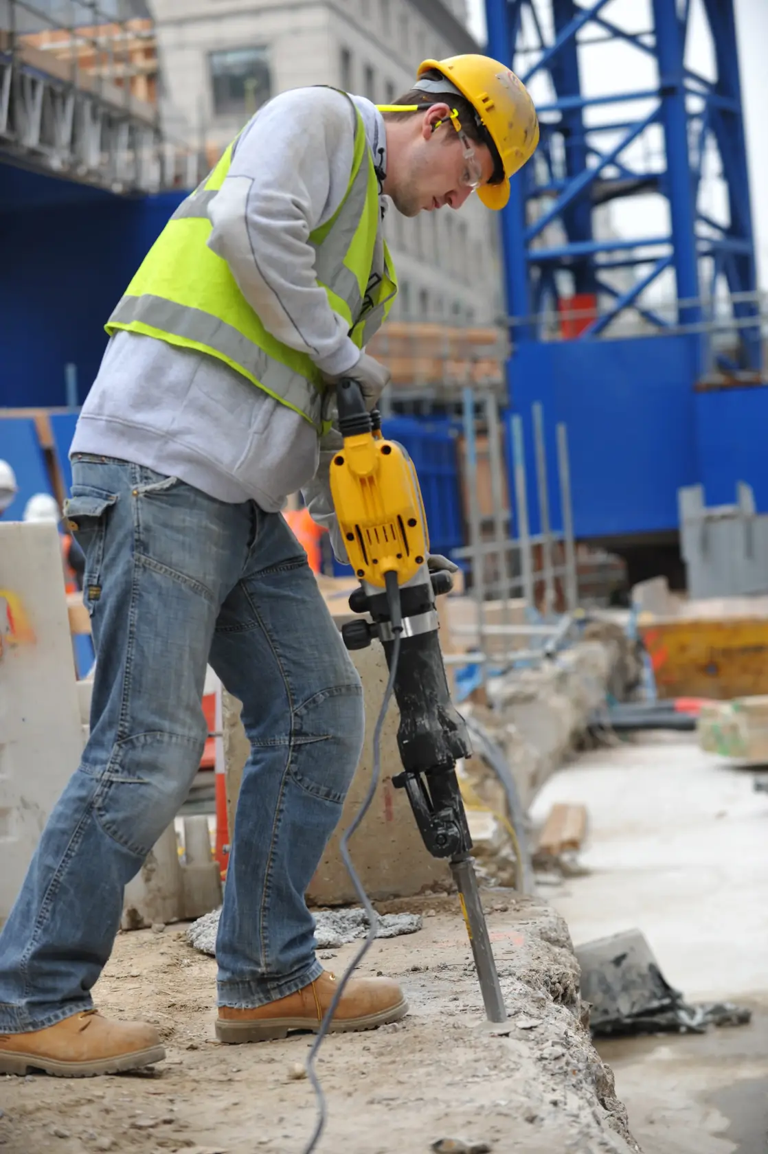 Ouvrier utilise un marteau-piqueur DEWALT D25960K sur béton, chantier, équipé de protection.