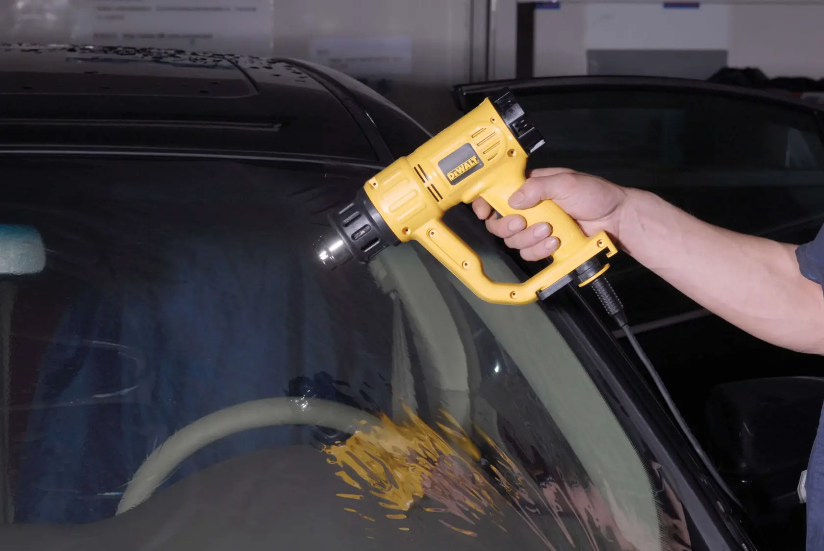 Une personne utilise un pistolet à air chaud DEWALT (modèle D26411) pour appliquer de la chaleur sur le pare-brise d'une voiture.