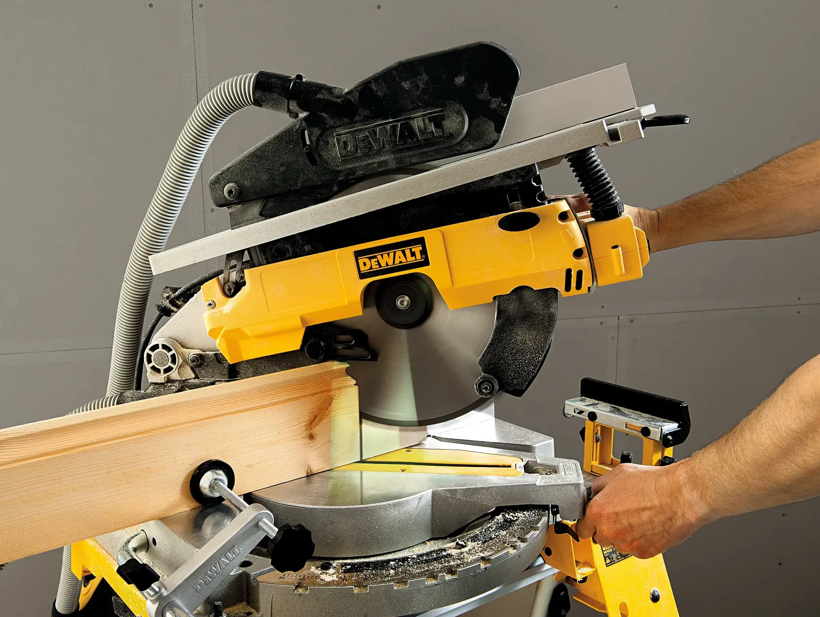 Une personne utilise une scie à onglets radiale DEWALT (modèle D27113) pour couper une pièce de bois. La scie est jaune et fixée sur un établi.