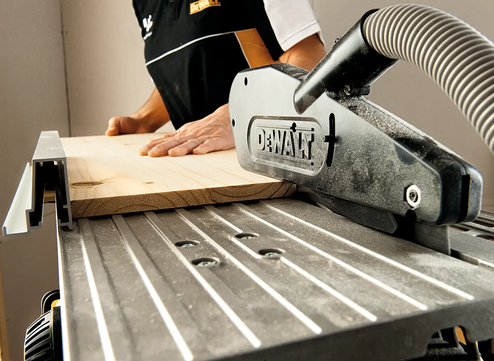 Vue rapprochée d'une scie sur table DEWALT en cours d'utilisation, avec une personne guidant une pièce de bois à travers la scie dans un environnement d'atelier.