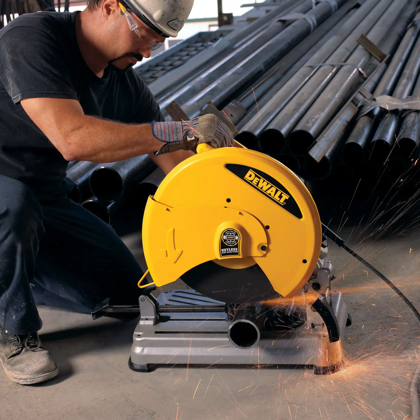 Un ouvrier utilise une scie à métaux jaune DEWALT D28715 pour couper un tuyau en acier, des étincelles volent, dans un environnement industriel avec des tuyaux empilés en arrière-plan.