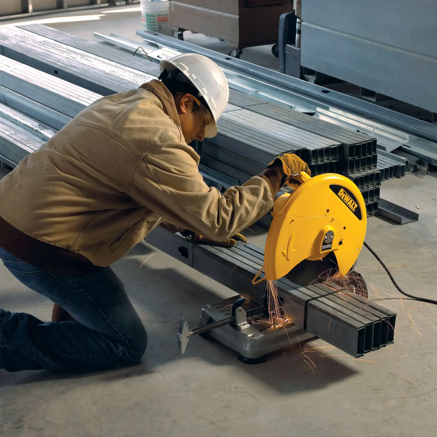 Une personne portant des équipements de sécurité utilise une scie à métaux DEWALT pour couper des tuyaux en acier dans un environnement industriel. Des étincelles sont visibles pendant le fonctionnement de la scie.