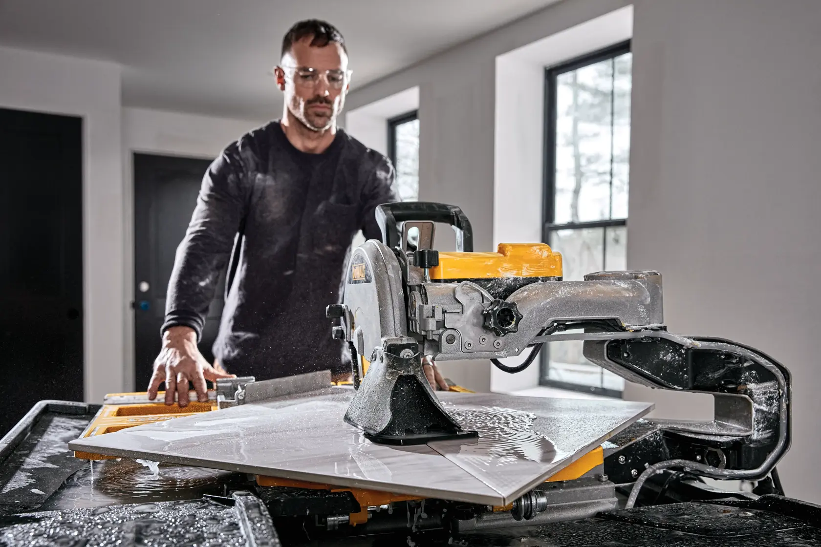 Eine Person bedient eine DEWALT D36000-QS Nassfliesensäge in einem hellen Raum und schneidet eine große Fliese, während Wasser auf die Arbeitsfläche spritzt.