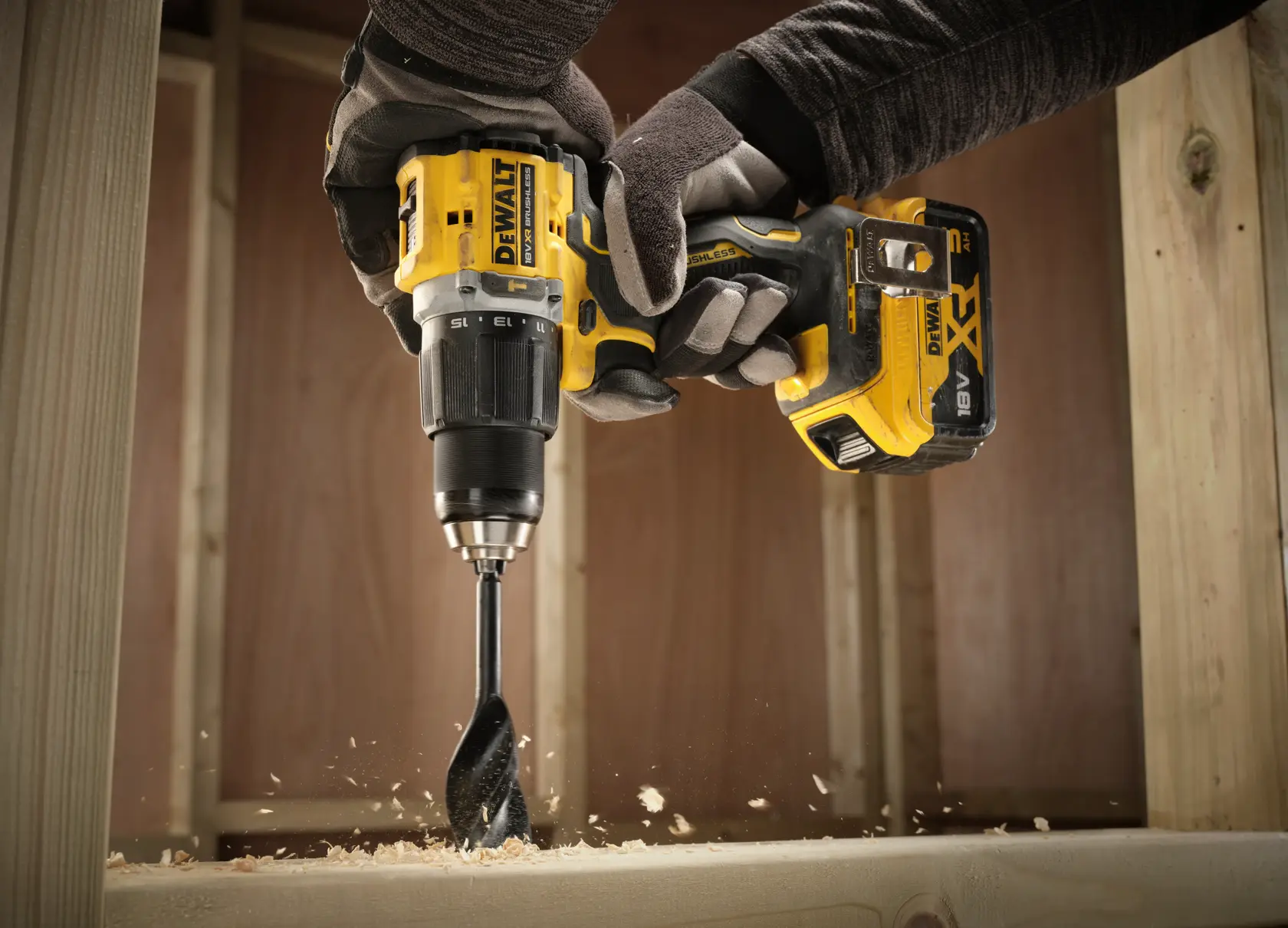 Manos con guantes usan un taladro inalámbrico DEWALT para perforar madera y crear virutas.