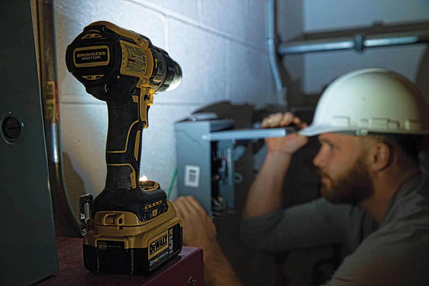 Une personne portant une veste haute visibilité et un casque de chantier utilise une perceuse-visseuse sans fil DEWALT (modèle DCD996P2) pour percer un mur en béton ou en maçonnerie dans un environnement industriel ou de construction. Le produit et la prise en main de l’outil sont clairement visibles.