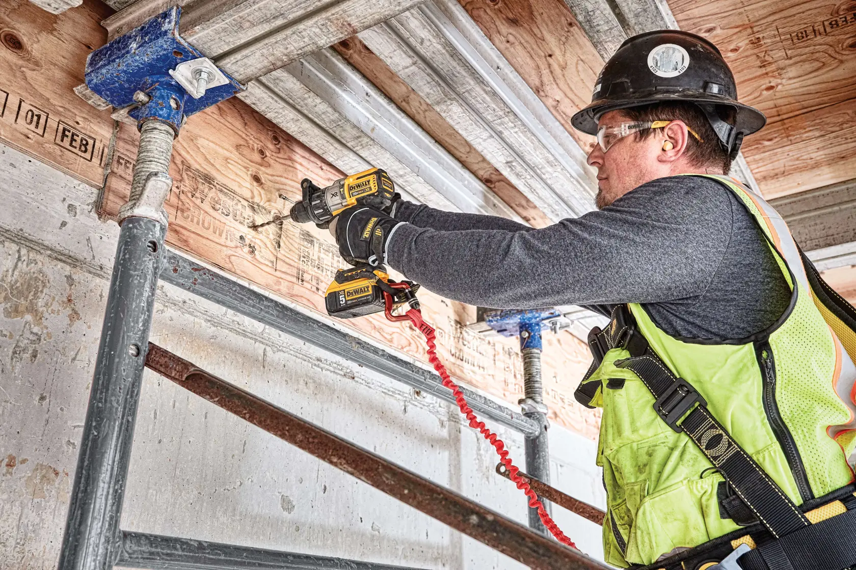 Une personne utilise une perceuse sans fil DEWALT (modèle DCD996P2) pour percer une poutre en bois sur un chantier de construction.