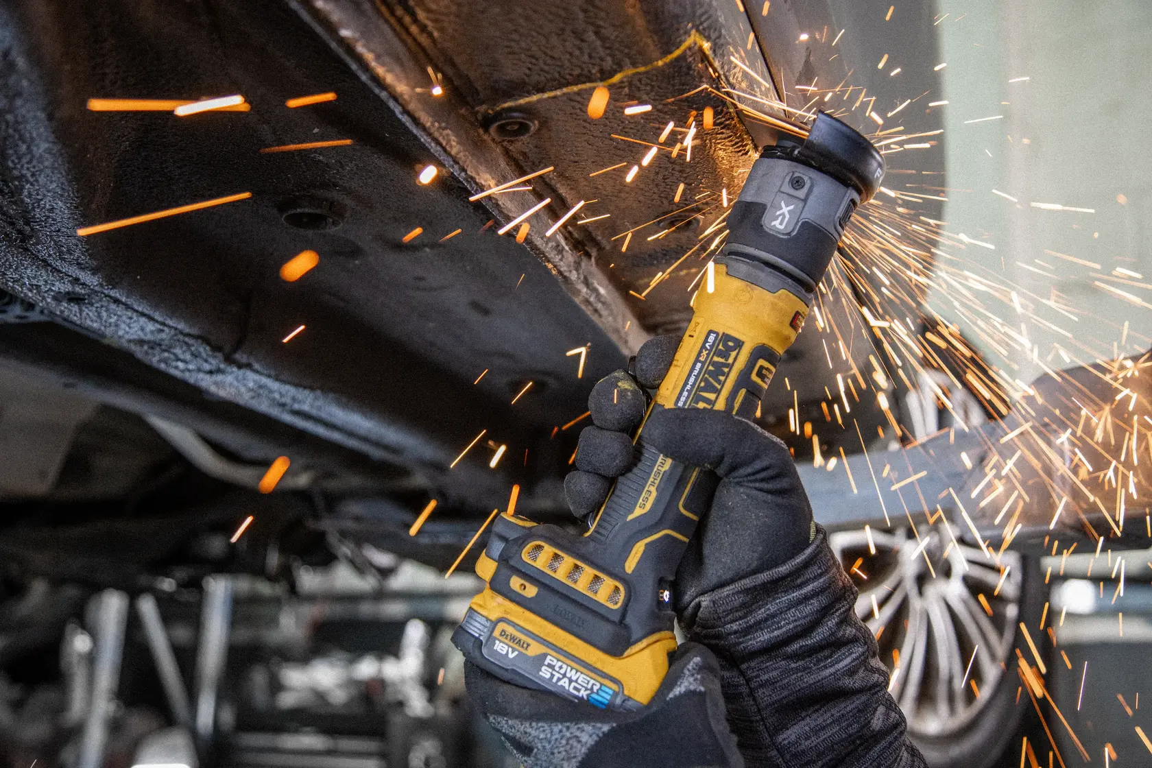 Meuleuse sans fil DEWALT produisant des étincelles lors de la découpe de métal sous un véhicule, main gantée.
