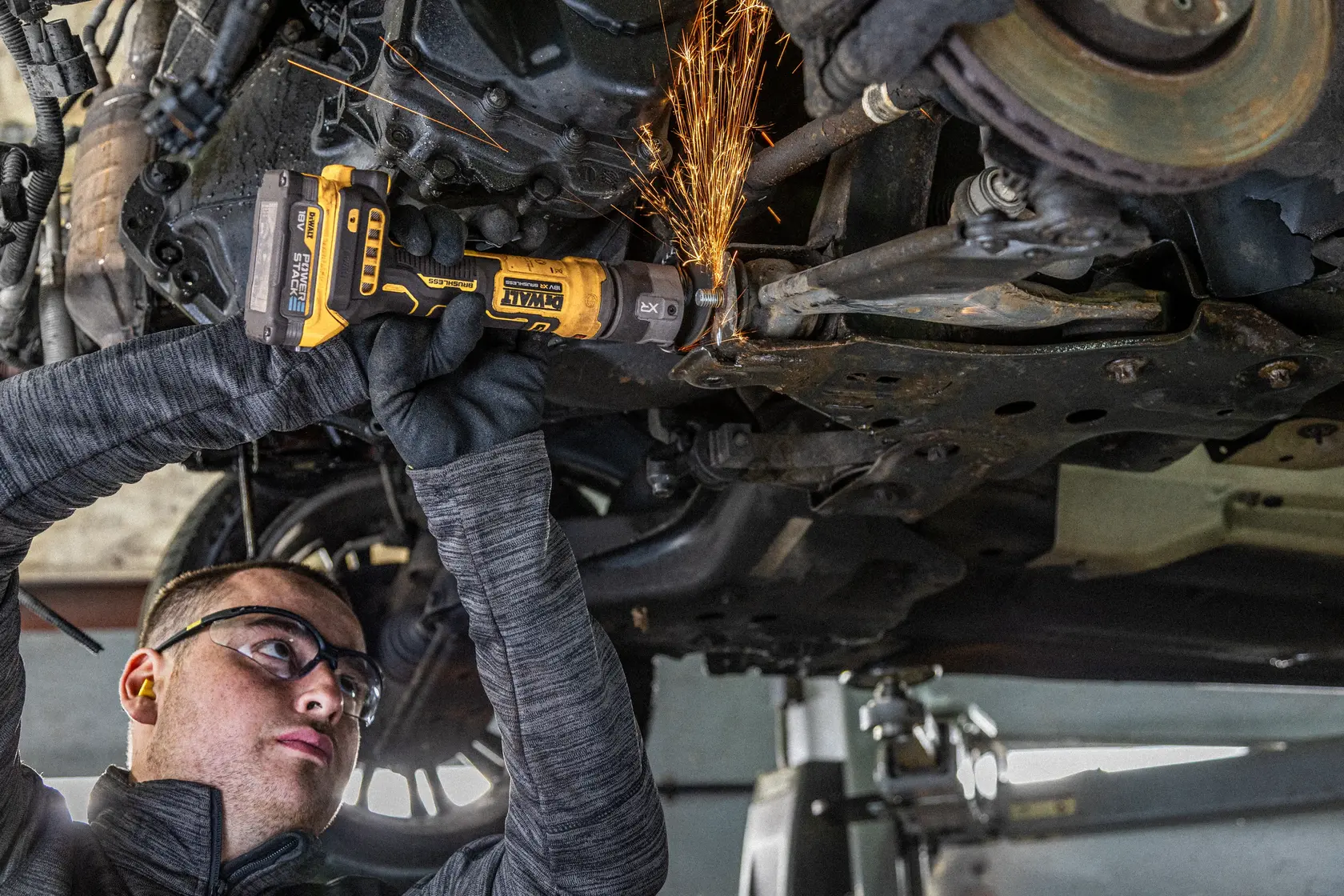 Personne utilisant une meuleuse DEWALT sous une voiture, coupant du métal avec des étincelles.