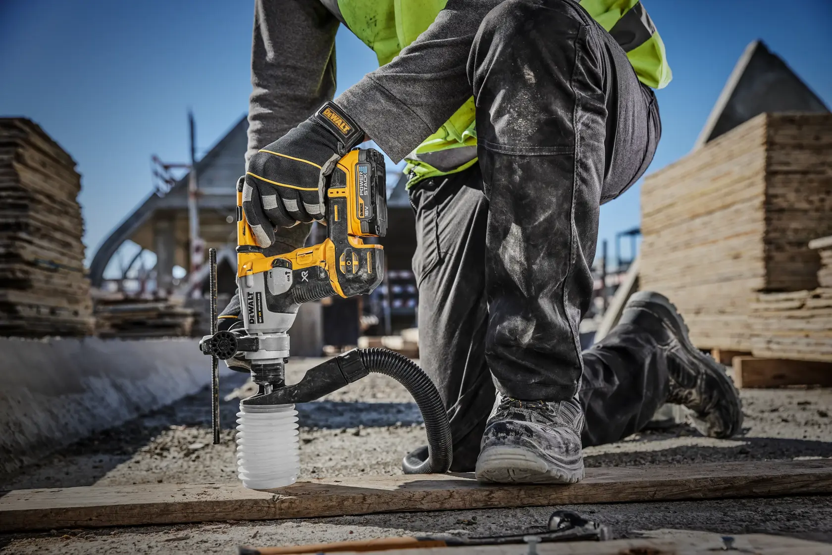 Un ouvrier du bâtiment utilise une perceuse perforatrice sans fil DEWALT (modèle DCH172E2T) avec extraction de poussière sur un chantier, perçant le sol à genou.