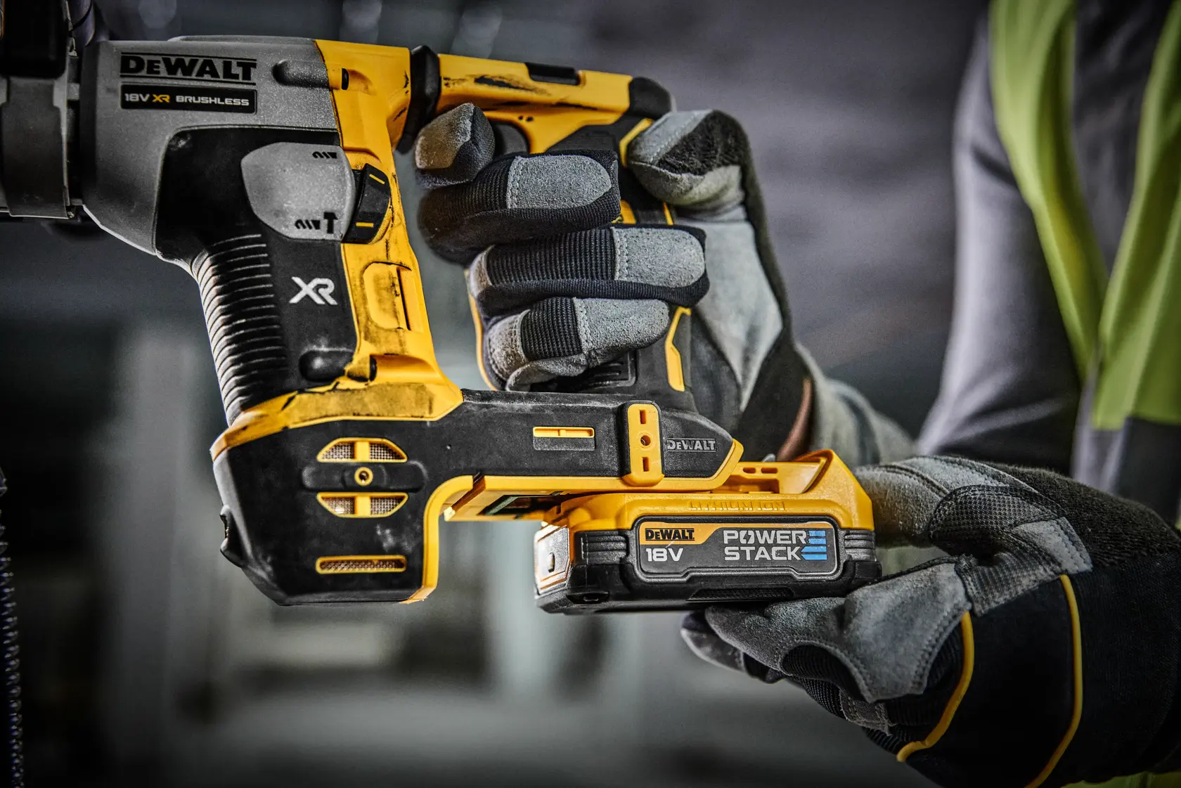 Gros plan sur une personne portant des gants de travail tenant un outil électrique DEWALT 18V XR brushless avec une batterie Power Stack dans un environnement d'atelier ou de chantier.