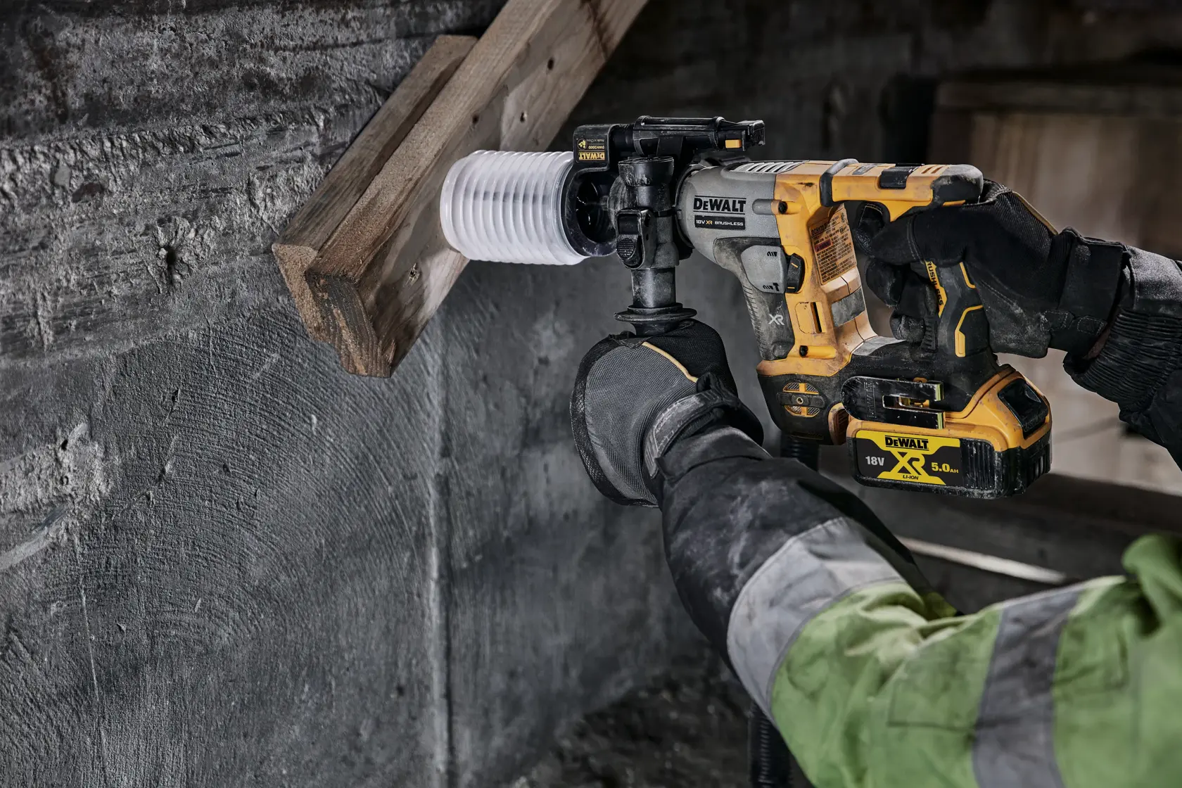 Marteau perforateur DEWALT sans fil, utilisé par un ouvrier en gants et veste verte, perçant bois et béton.