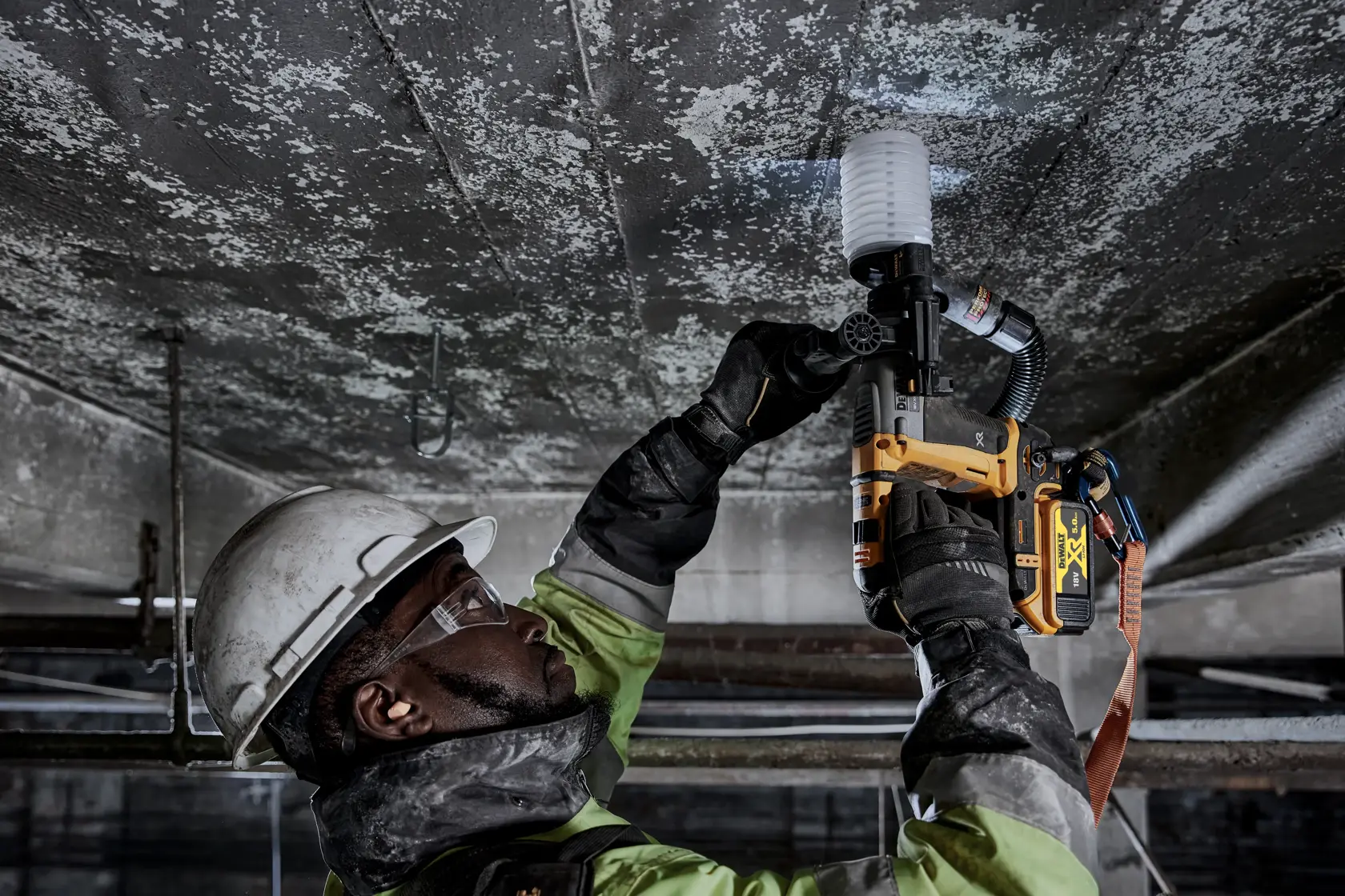 Ouvrier utilise une DEWALT DCH172P2 sur un plafond, équipé de protections, dans un environnement industriel.