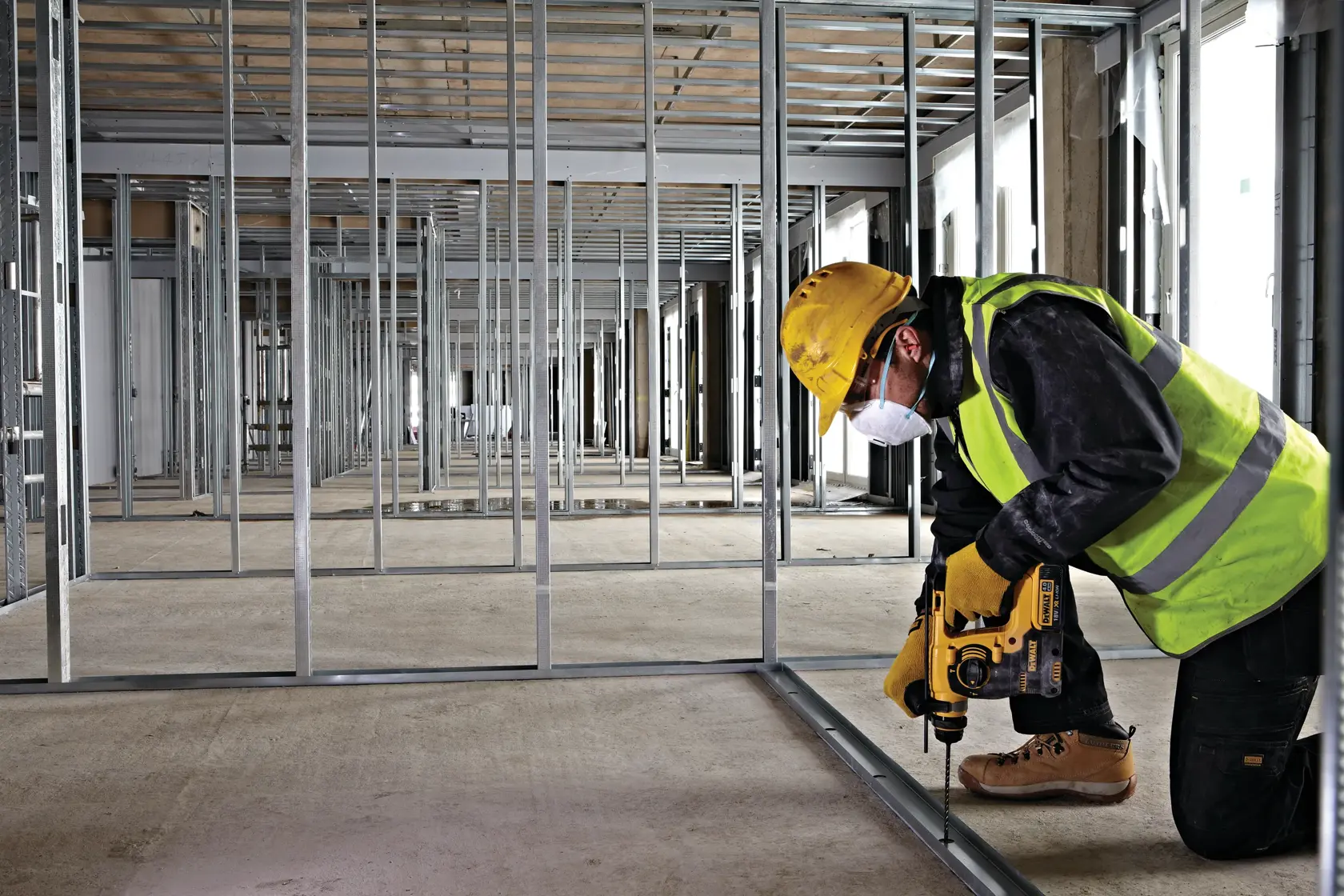 Operario usa herramienta DEWALT para perforar marco metálico, con equipo de seguridad en obra.