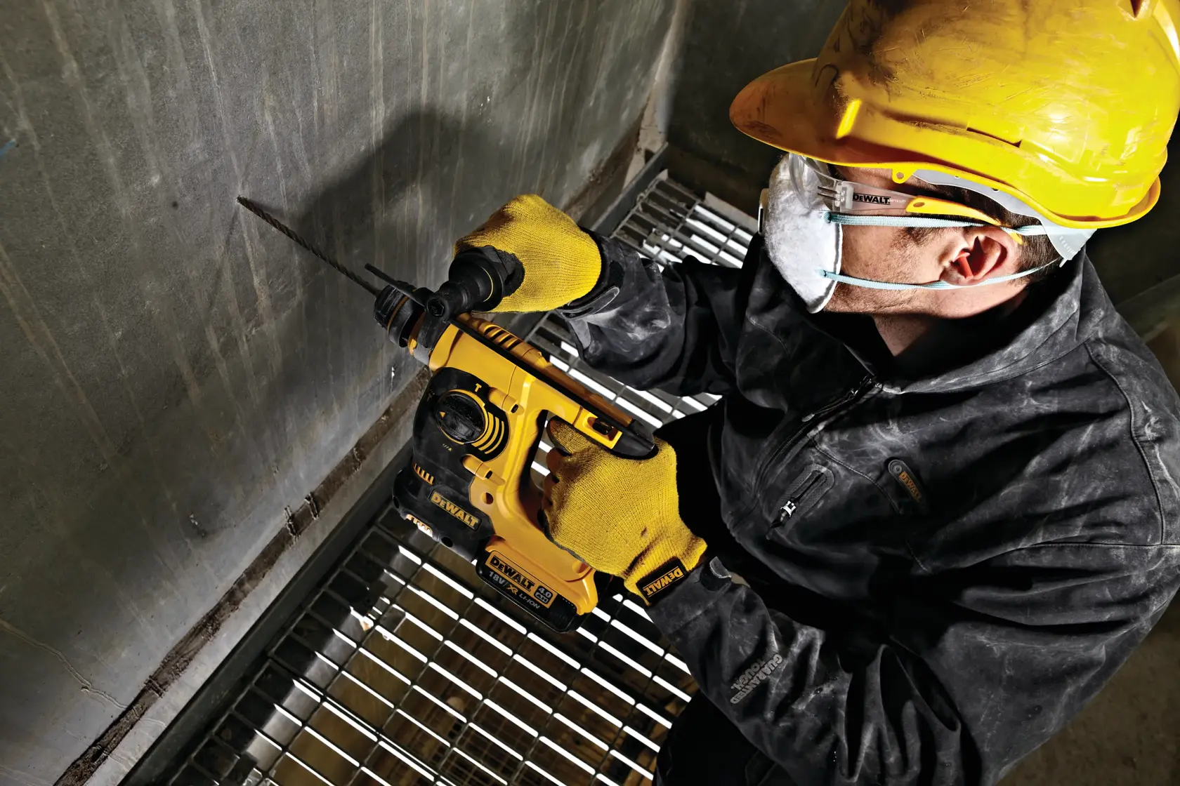 Trabajador usa un martillo rotativo DEWALT DCH253N en pared de concreto, con equipo de seguridad.