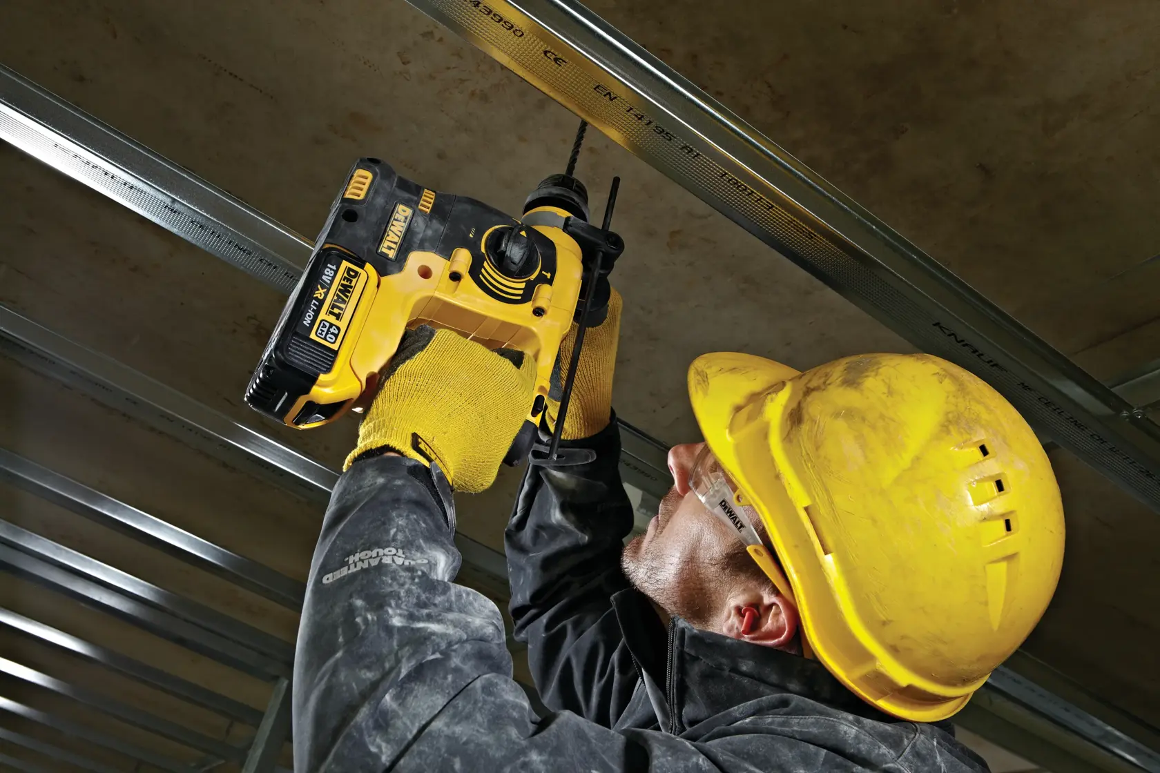 Persona con equipo de seguridad usa DEWALT DCH253N para perforar una estructura de techo en obra.