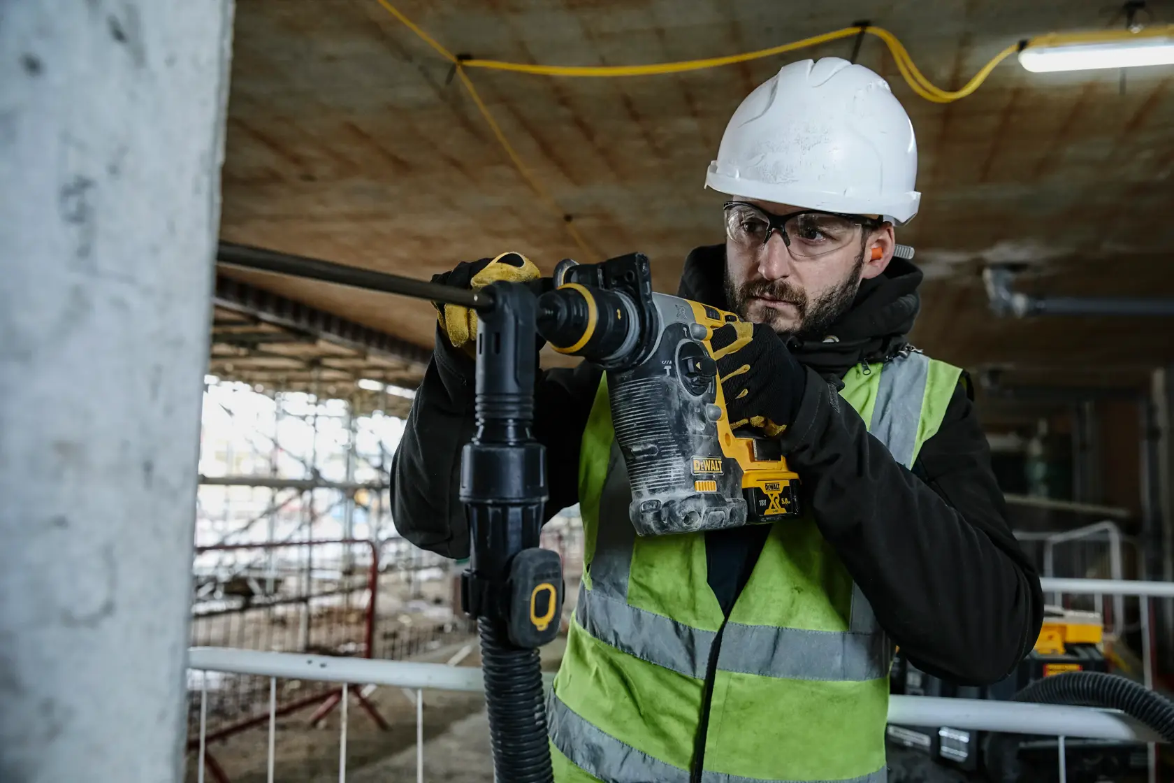 Arbeiter nutzt einen DEWALT Bohrhammer auf Baustelle, mit Helm, Handschuhen und Sicherheitsweste.