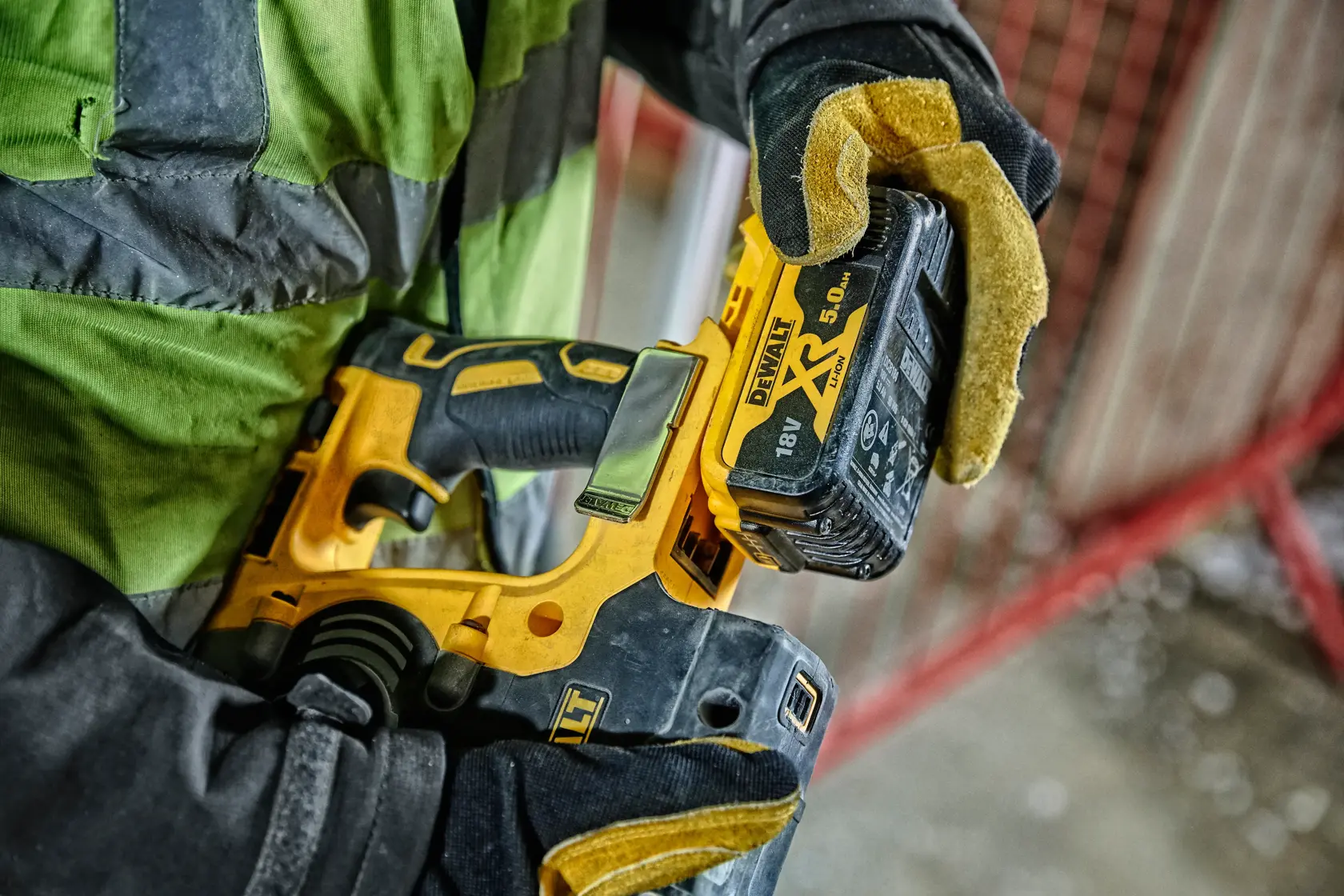 Hand mit Handschuh hält DEWALT DCH274P2T Akku-Werkzeug mit 18V XR-Batterie auf Baustelle.