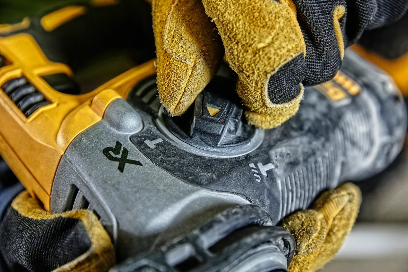 Hand im Handschuh stellt Regler an gelbem DEWALT Elektrowerkzeug mit Funktionssymbolen ein.