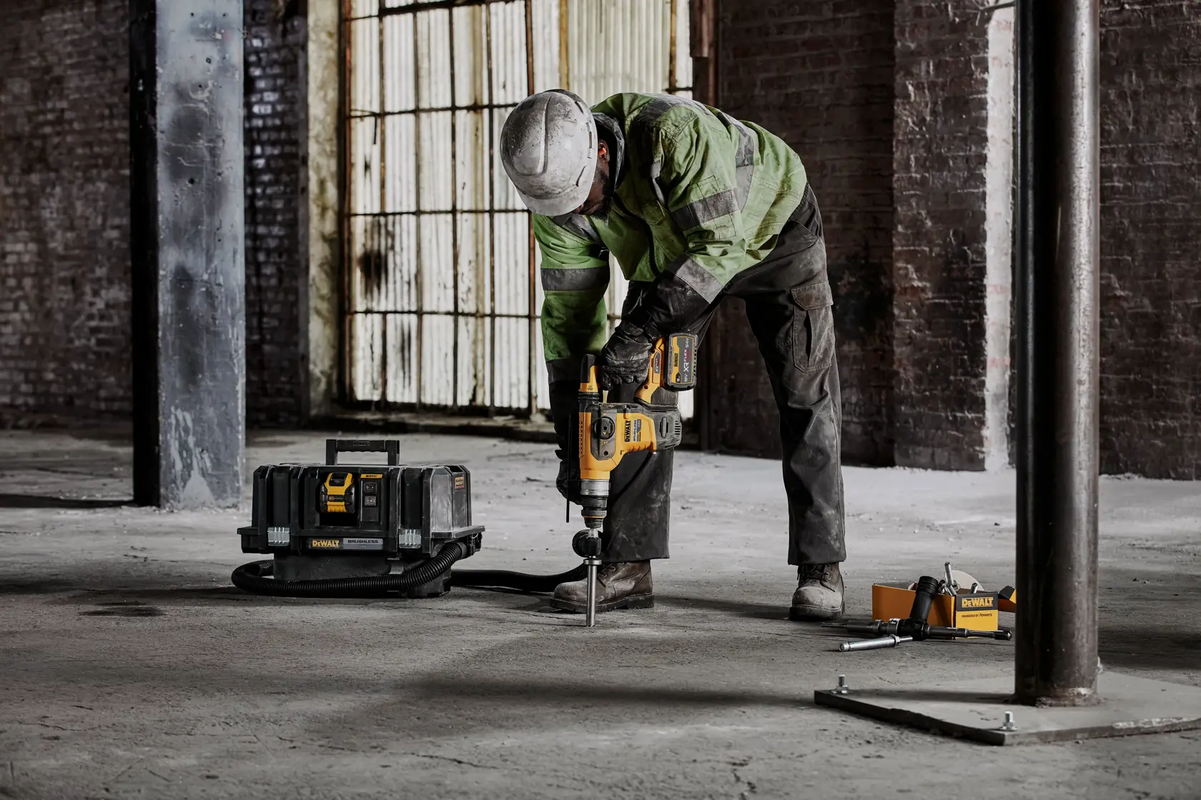 Person nutzt DEWALT Bohrhammer auf Betonboden, Werkzeugkoffer in der Nähe auf Baustelle.
