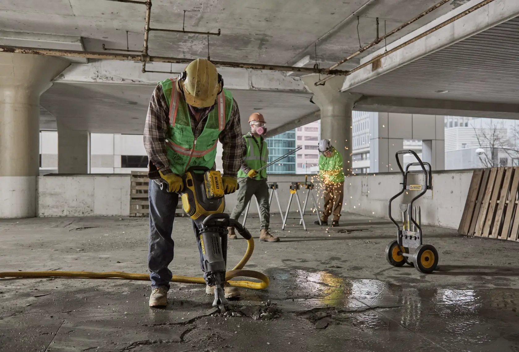 Des ouvriers utilisent des outils DEWALT sur un chantier, dont un marteau-piqueur et un chariot d'équipement.