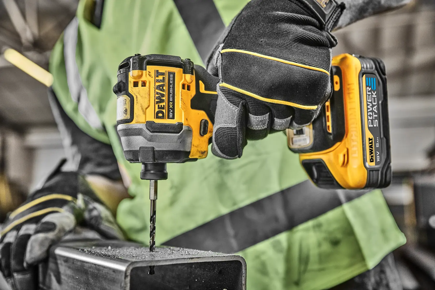 Main gantée utilisant une perceuse sans fil DEWALT pour percer une poutre métallique sur un chantier.
