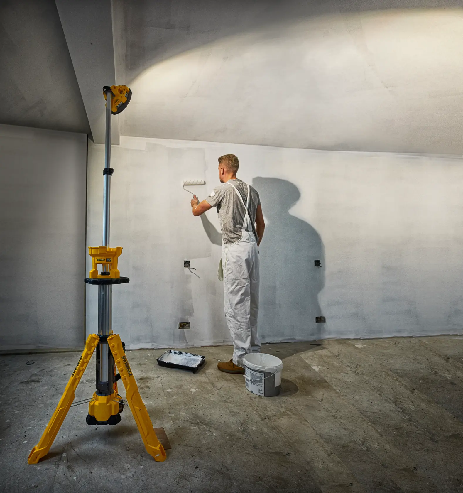 Photo du projecteur DEWALT DCL079-XJ, DCL079 sur trépied éclairant un peintre à l’intérieur.