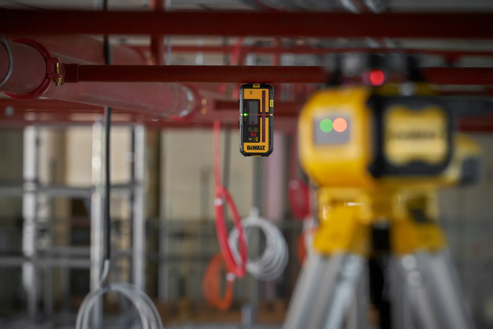 Détecteur laser DEWALT et trépied utilisés sur chantier avec tuyaux et câbles en arrière-plan.