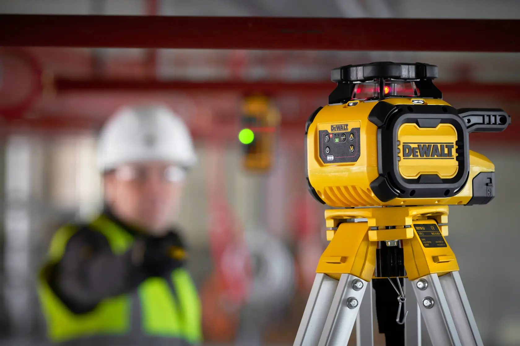 Laser DEWALT sur trépied, DCLE15211R et DCLE15211R-QW, chantier, travailleur flou.