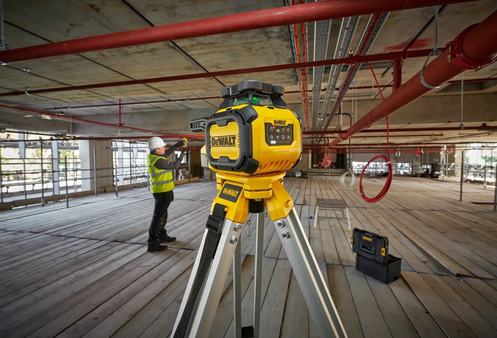 Outil photo DEWALT DCLE15221G-QW, DCLE15221G sur trépied chantier. Ouvrier et boîte à outils en arrière-plan.