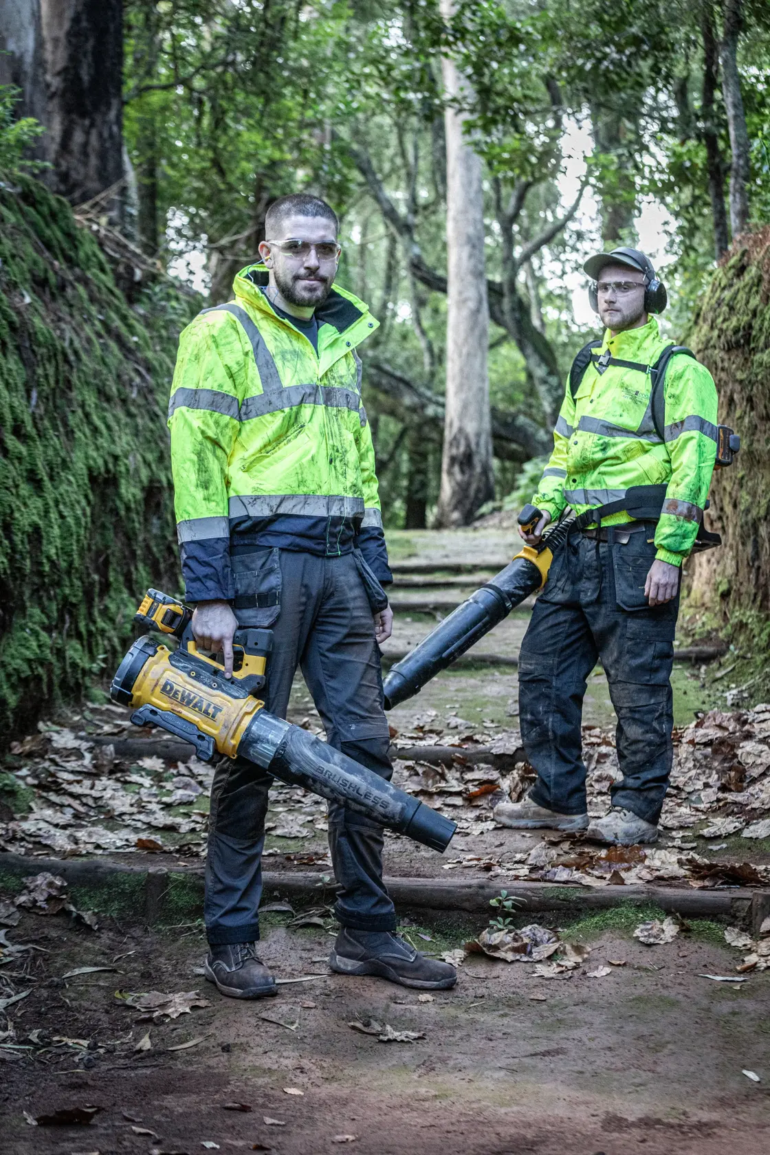 Deux personnes avec souffleurs DEWALT, DCMBBL800N-XJ, DCMBBL800N, vestes haute visibilité dehors.