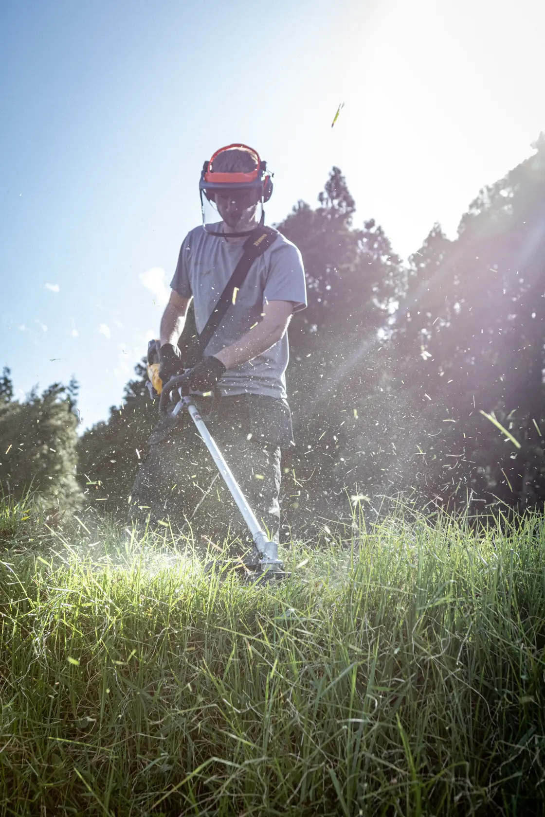 DEWALT DCMBC812N-XJ, DCMBC812N en action. Personne taille l’herbe dehors, équipement de protection porté.