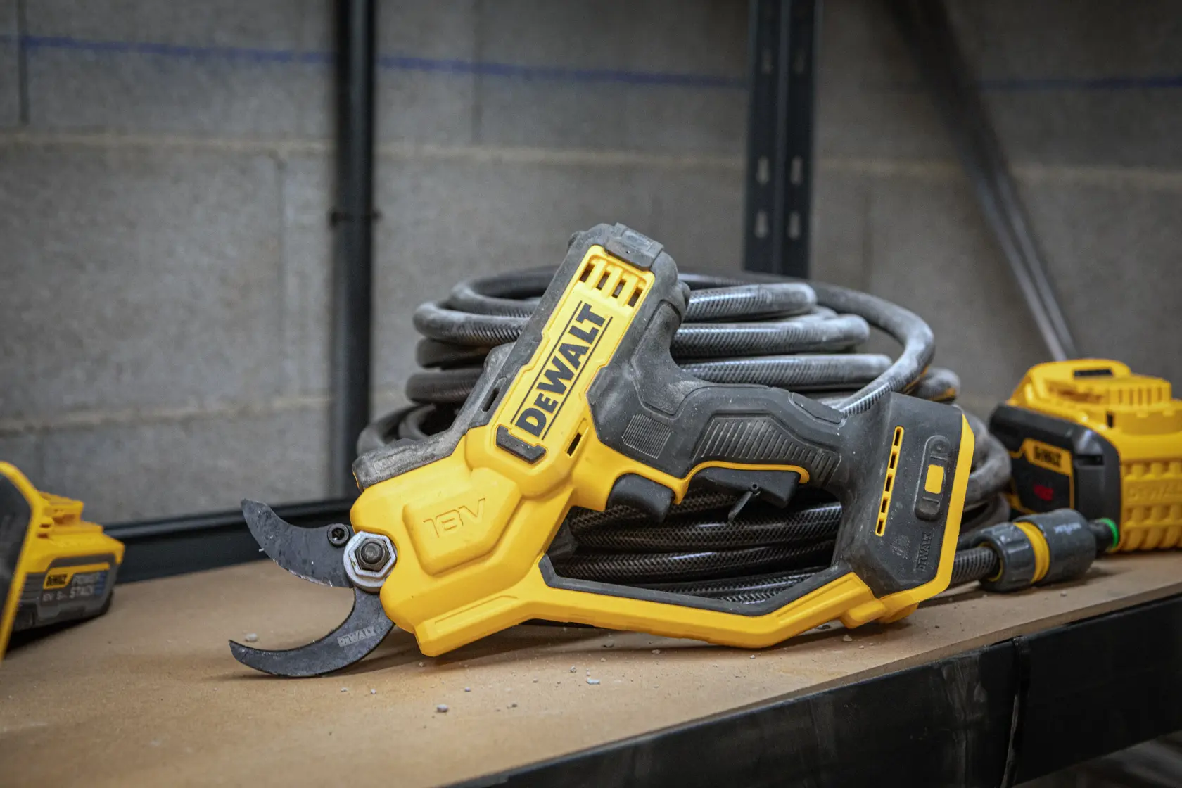 Sécateur sans fil DEWALT 18V sur un établi, à côté d’un tuyau et d’autres outils.