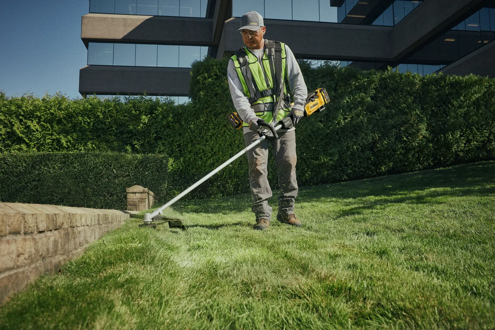 Une personne coupe l’herbe avec une DEWALT DCMST901N sans fil près d’une bordure en brique.