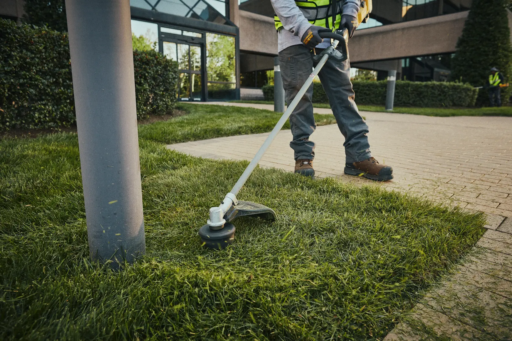 Personne utilisant un coupe-bordure DEWALT sans fil près du trottoir et du lampadaire dehors.