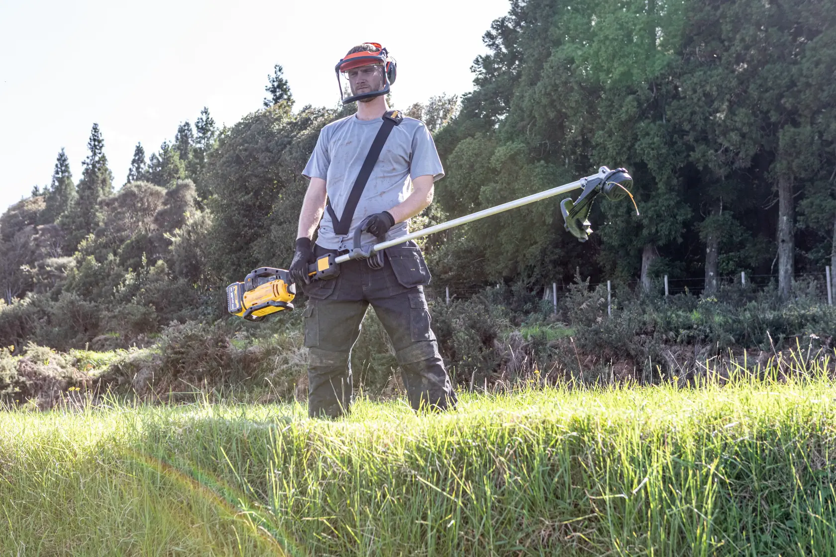 Personne utilise coupe-herbe DEWALT DCMST911N et DCMST911N-XJ dehors avec équipement de protection.