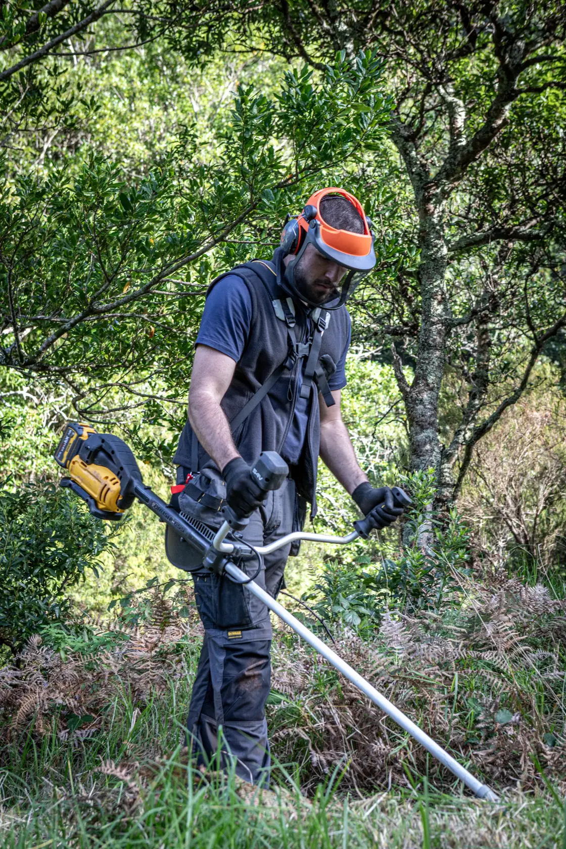 Personne avec coupe-herbe DEWALT, DCMST922N, DCMST922N-XJ, en extérieur avec équipement de sécurité.