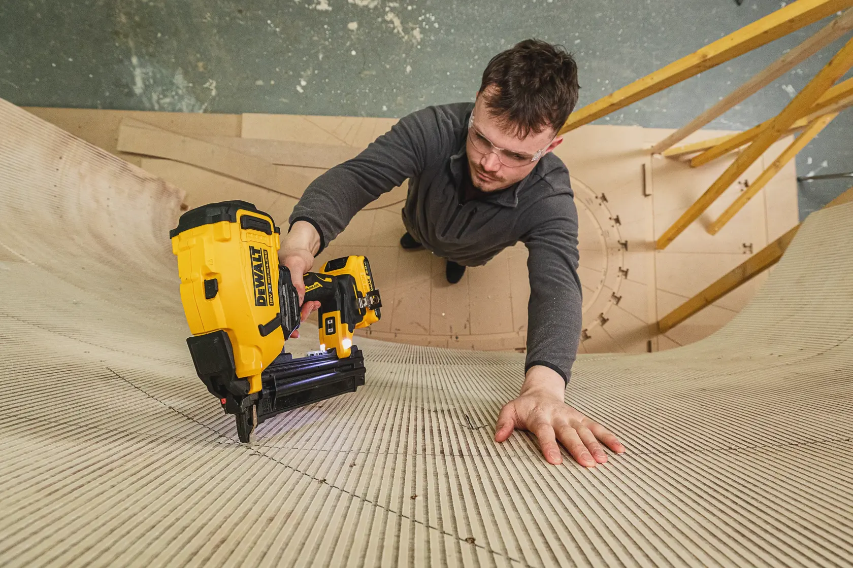 Personne utilisant une cloueuse DEWALT DCN210SN-XJ pour fixer des panneaux de bois courbés en atelier.