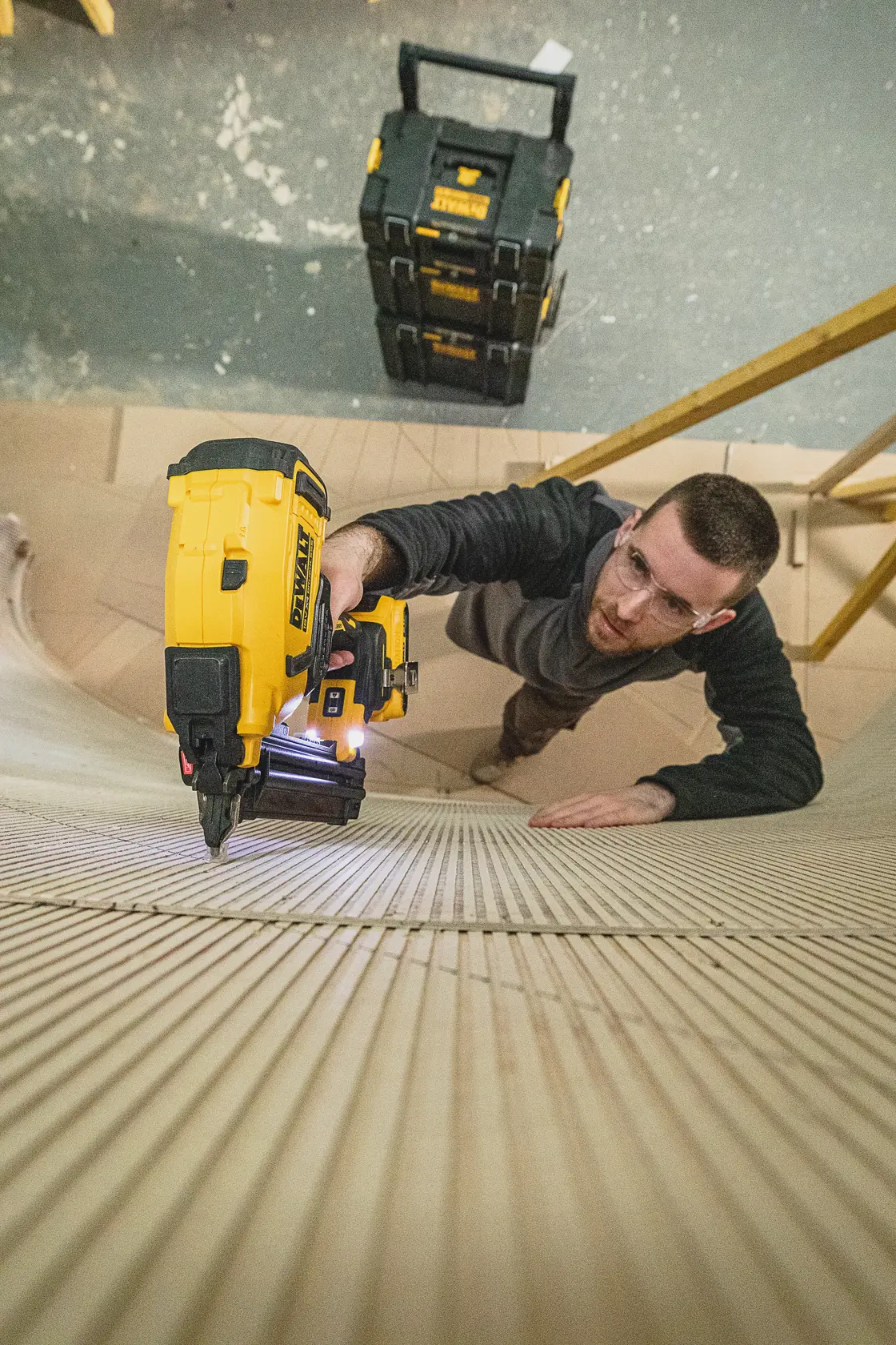 Personne utilisant un cloueur DEWALT sur une surface en bois, coffres DEWALT visibles à l’arrière-plan.