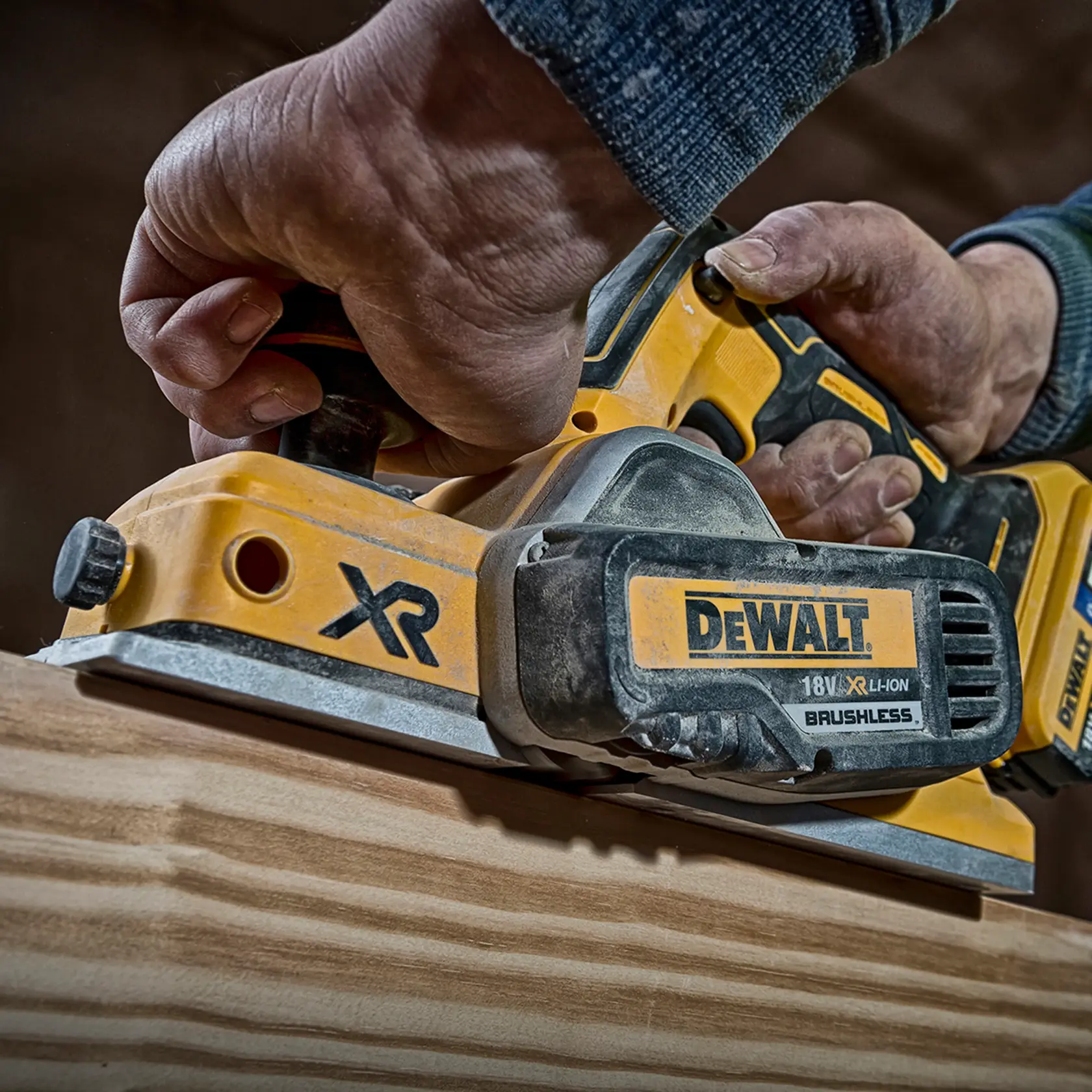 Main utilisant une raboteuse DEWALT DCP580P2 sans fil pour lisser du bois. Vue rapprochée.