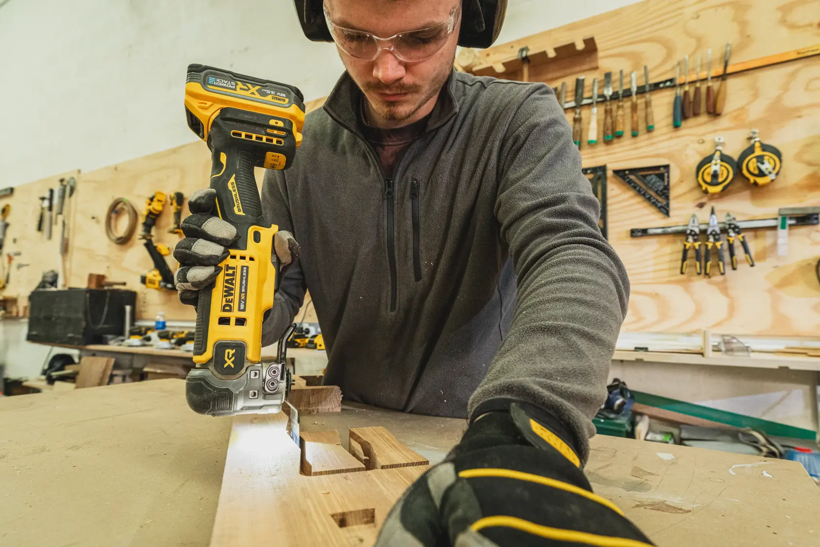 Une personne utilise une scie sans fil DEWALT DCS359N-XJ pour découper du bois sur un établi en atelier.
