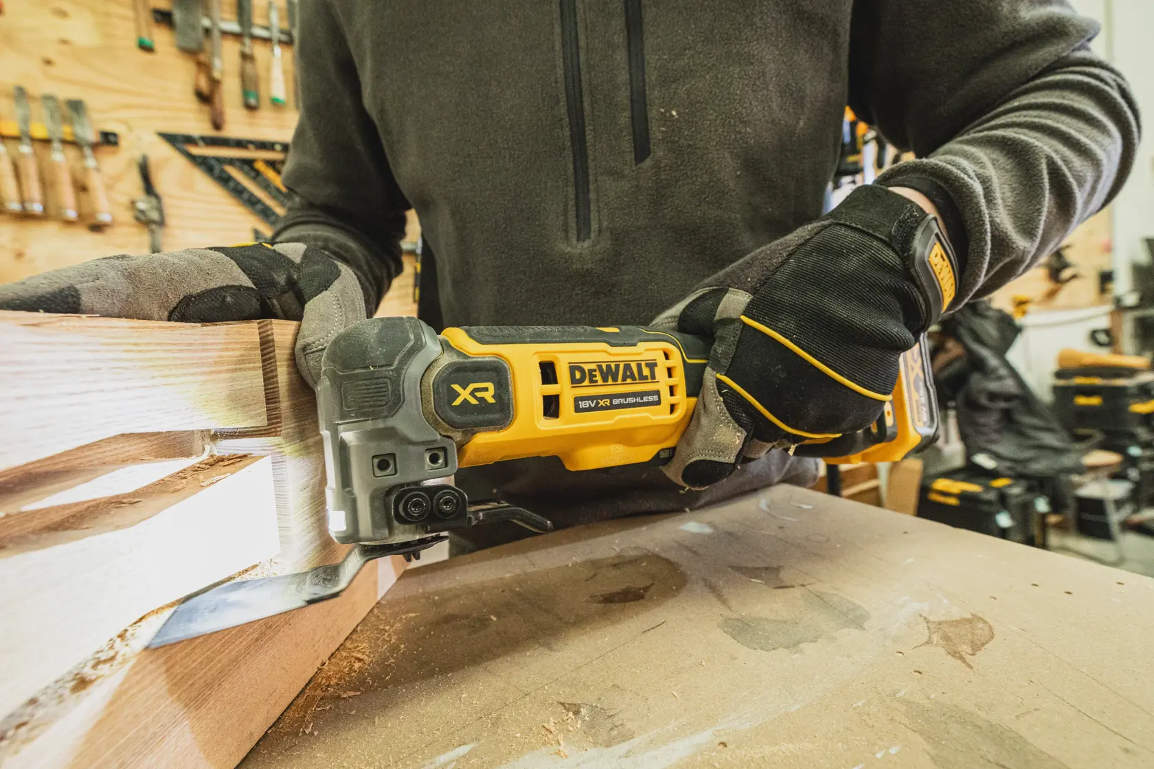 Personne utilisant un outil DEWALT XR sans balais pour couper du bois, portant des gants en atelier.