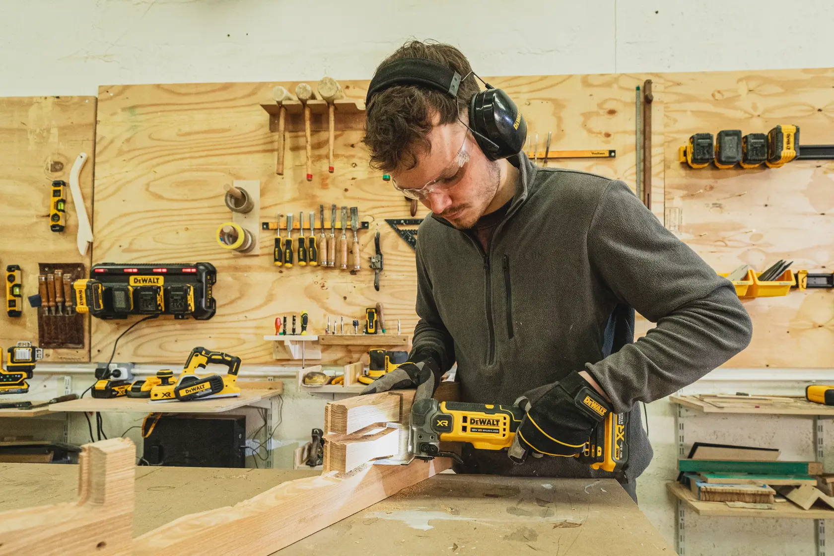 Personne utilisant un outil DEWALT DCS359N-XJ sur du bois dans un atelier, équipée de protections.