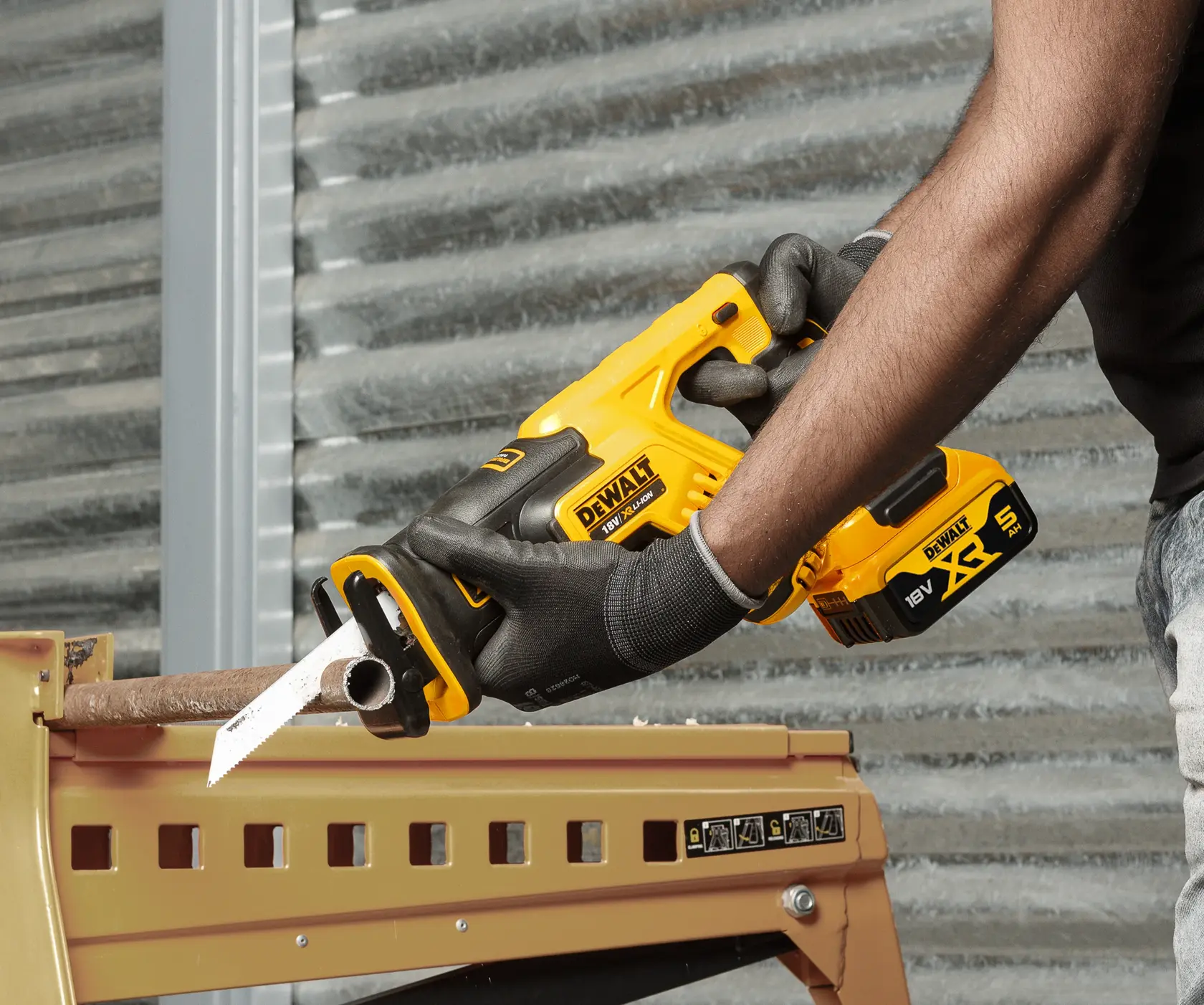 Une personne coupe un tuyau en métal avec une scie sabre sans fil DEWALT, portant des gants.