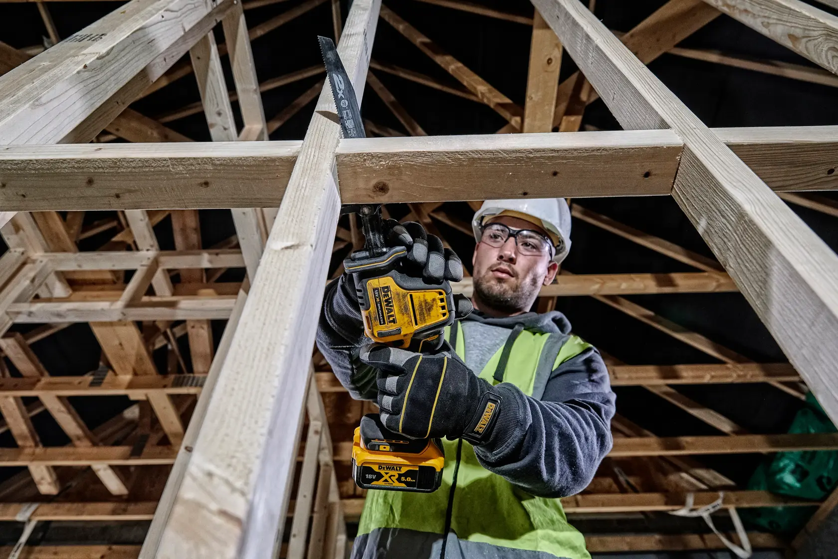 Photo de la scie sabre sans fil DEWALT DCS369P2 utilisée sur une charpente en bois par un ouvrier équipé de sécurité.