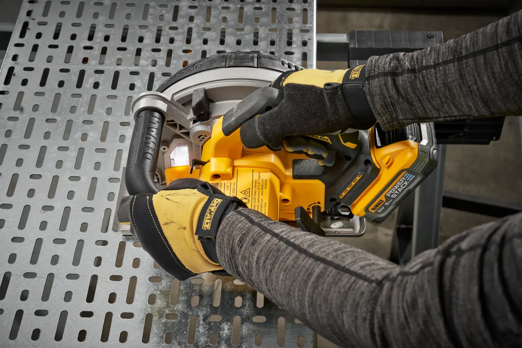 Hands using a DEWALT cordless reciprocating saw on a metal surface, wearing protective gloves and work gear.