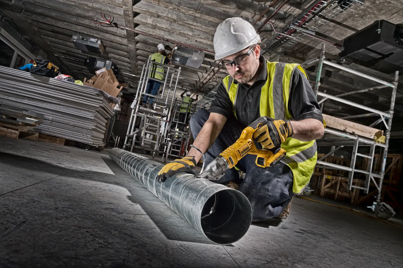 DEWALT DCS491NT-XJ et DCS491NT cisaille métal sur chantier, ouvrier coupe un tuyau, gilet haute visibilité, casque.