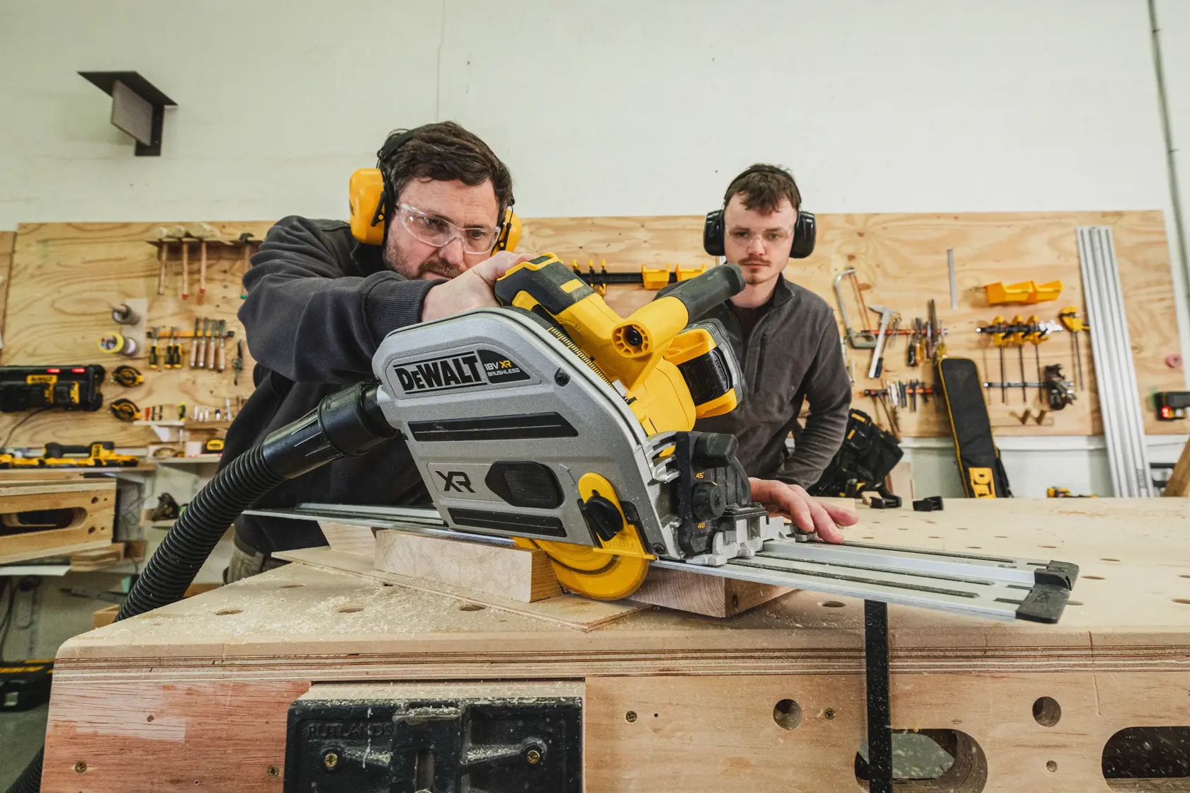 Zwei Personen schneiden Holz mit einer kabellosen DEWALT Führungssäge in einer Werkstatt.