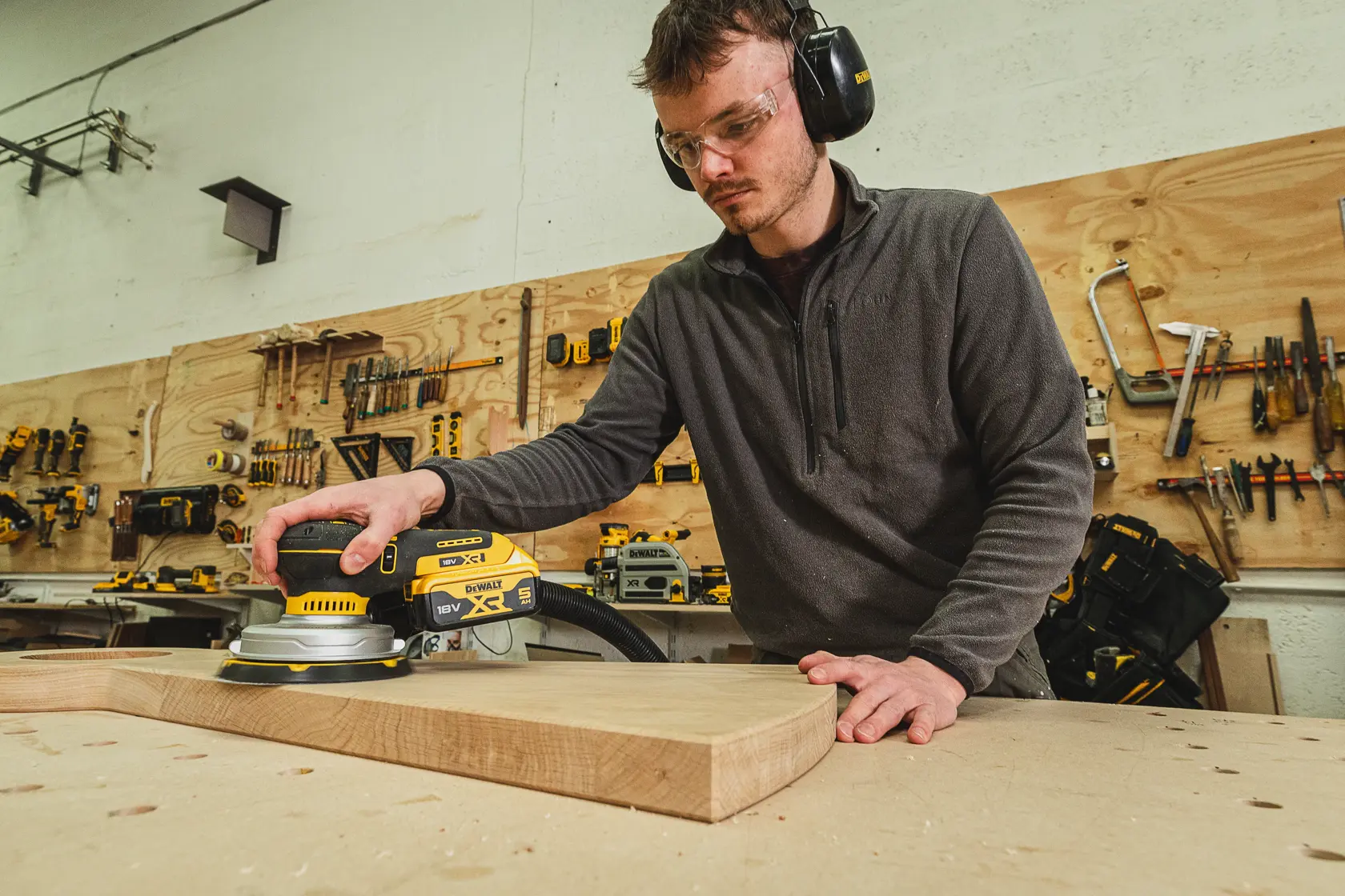Personne ponçant du bois avec une ponceuse DEWALT DCW230N-XJ dans un atelier en portant des équipements.